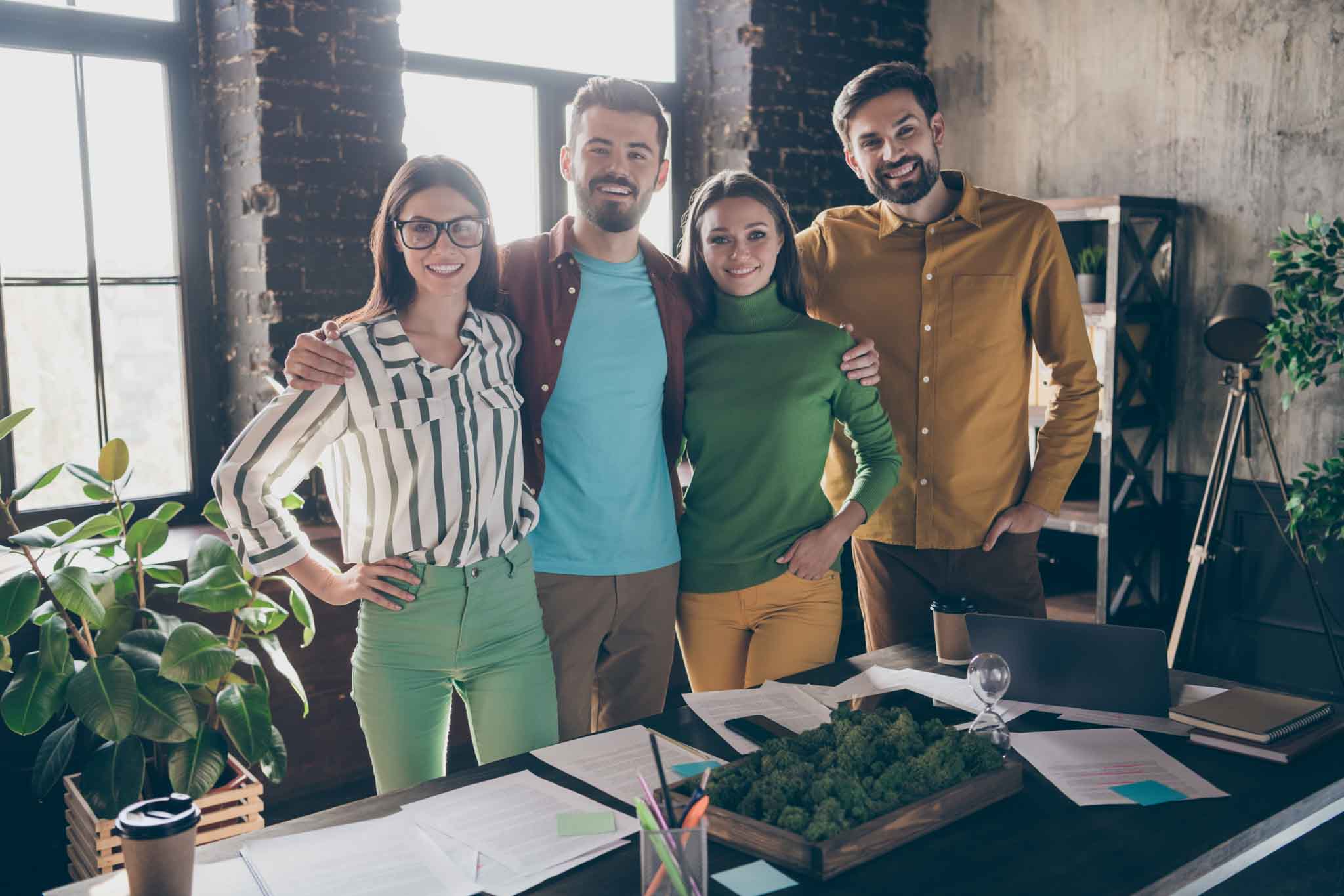 Company of four nice attractive friendly professional cheerful cheery, people leaders partners IT specialists hugging support corporate climate at work place station office indoors
