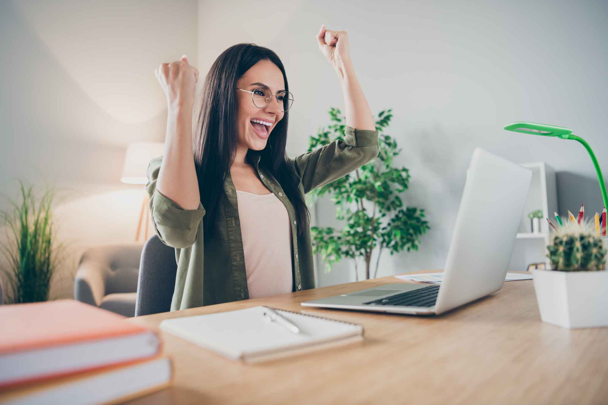 Photo of young happy positive excited crazy smiling cheerful woman in glasses work in laptop raise fists in victory at home.