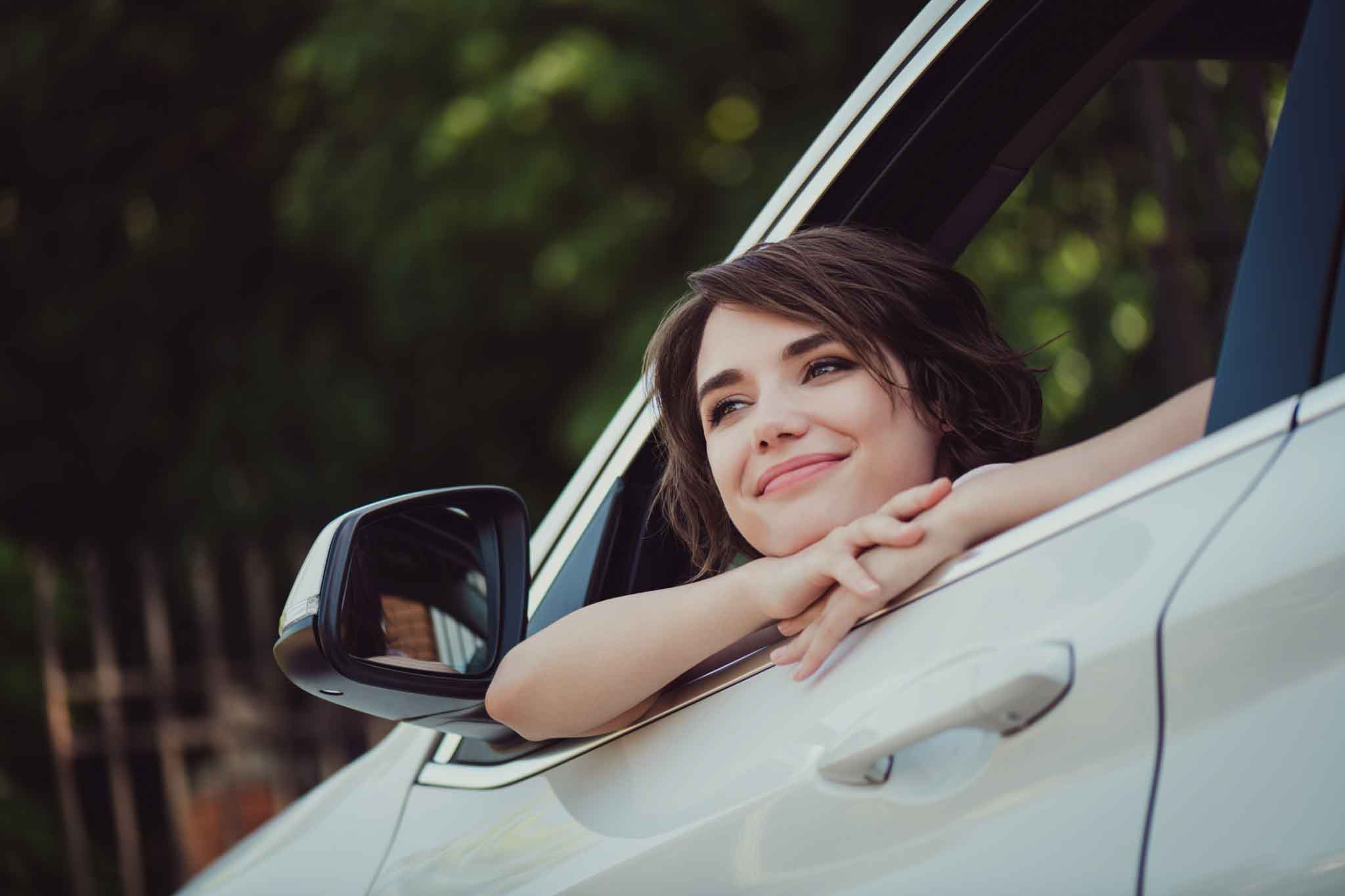 Photo of charming lovely lady smiling face hands chin dreamy inspired look, out of car rearview mirror handle relaxing enjoying natural view breathe fresh air wear white shirt indoors