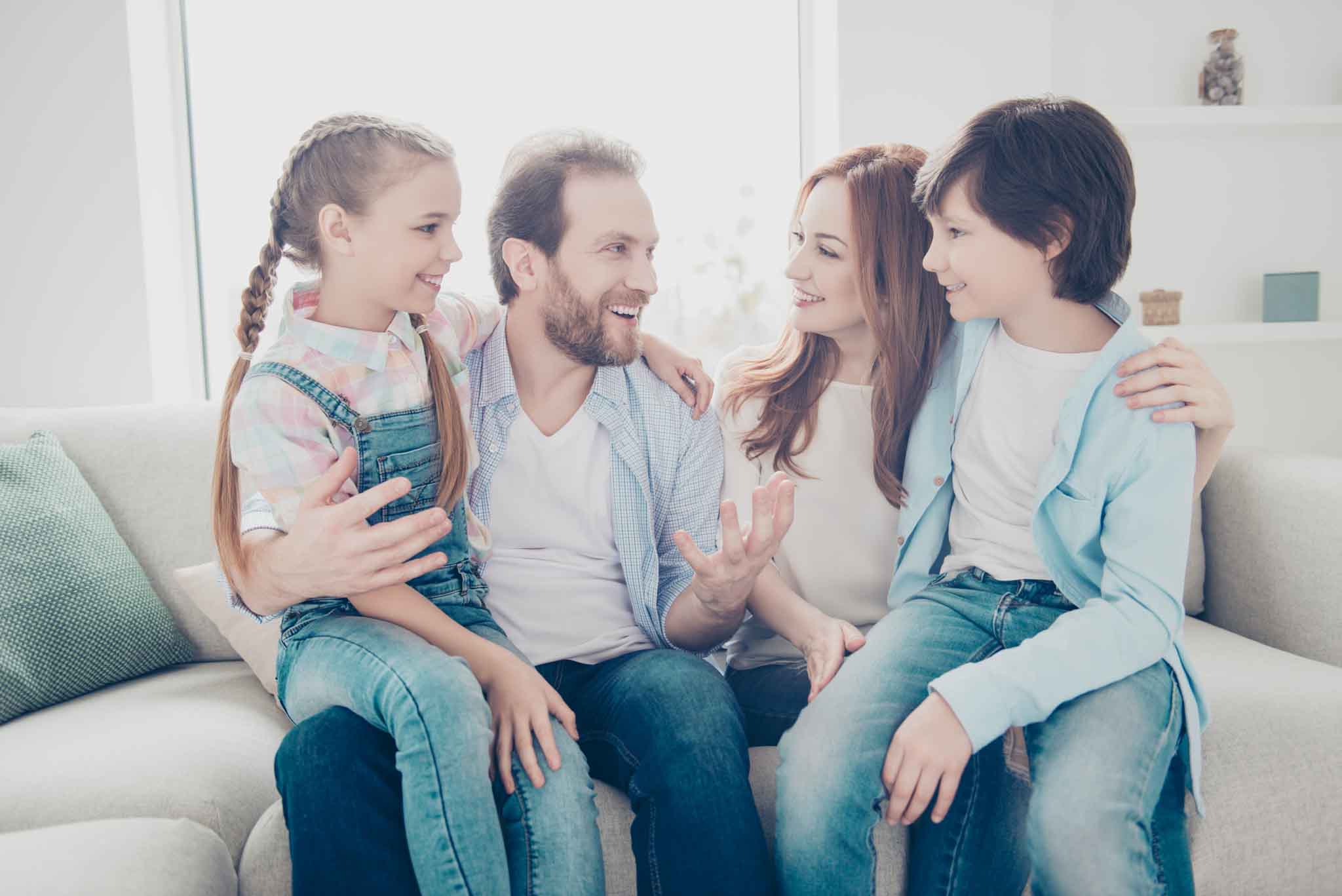 Portrait of cheerful dad with stubble telling joke to wife two kids, full family embracing, sitting on couch in living room, listening comic funny story,  daydream freetime concept