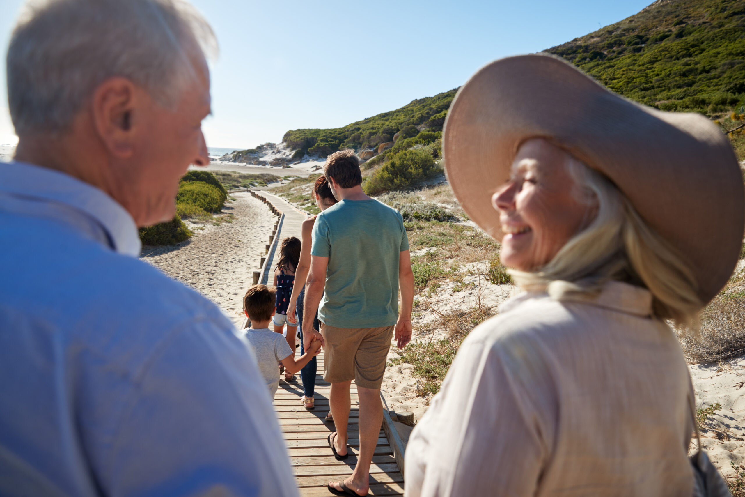 Three generation white family walking on a beach, grandparents in the foreground, over shoulder view