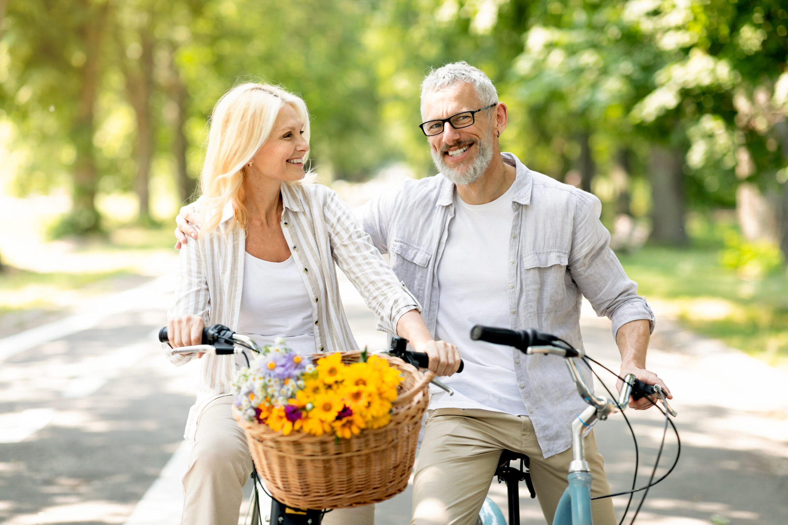 Portrait Of Happy Senior Spouses Having A Ride On Bicycles In Summer Park, Romantic Cheerful Mature Couple Spending Time Together Outdoors, Enjoying Active Lifestyle On Retirement, Copy Space