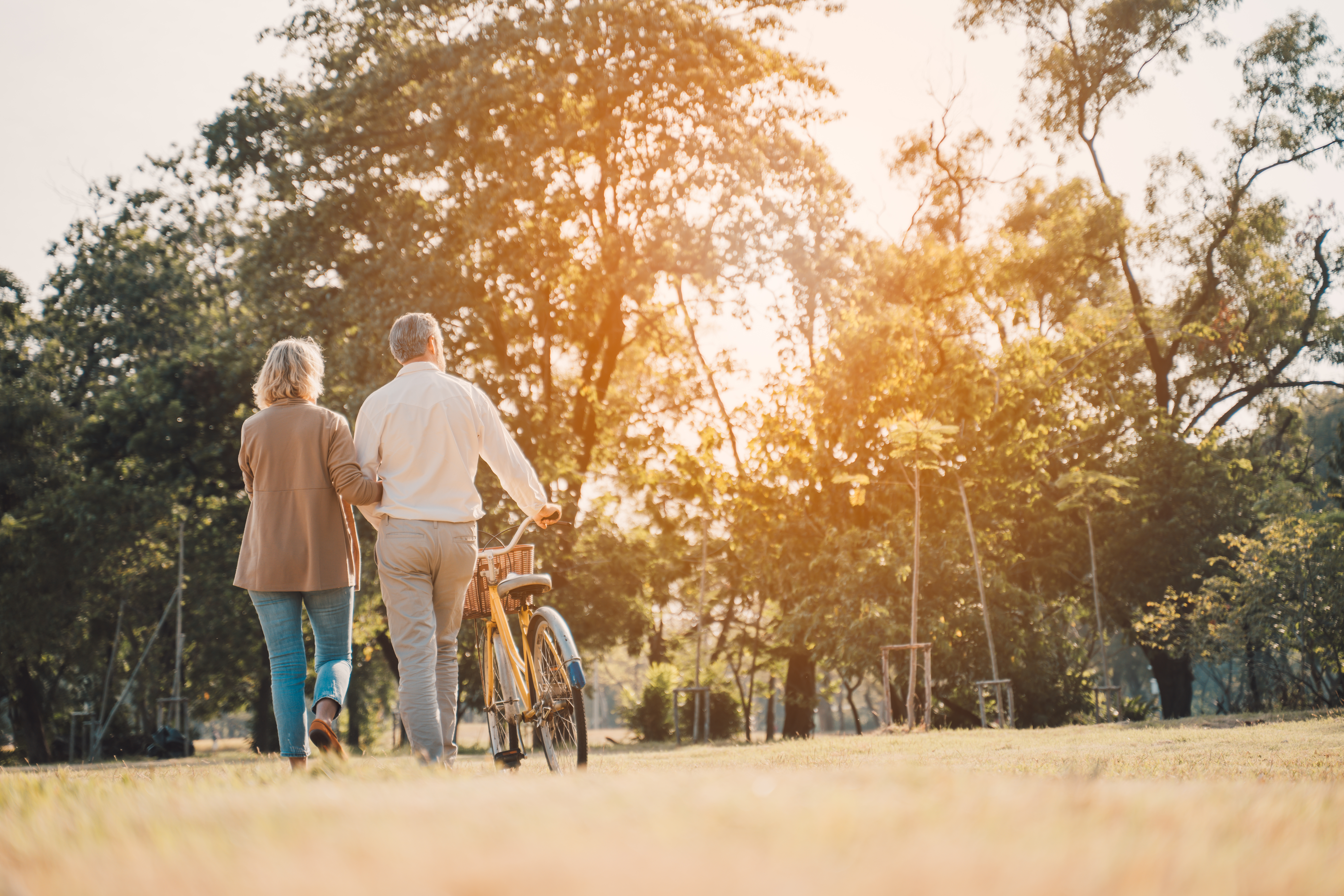 Beautiful Senior couple walking their bike along happily talking in park.mature couple in summer park.Elderly man and old woman with bicycles outside in spring nature.